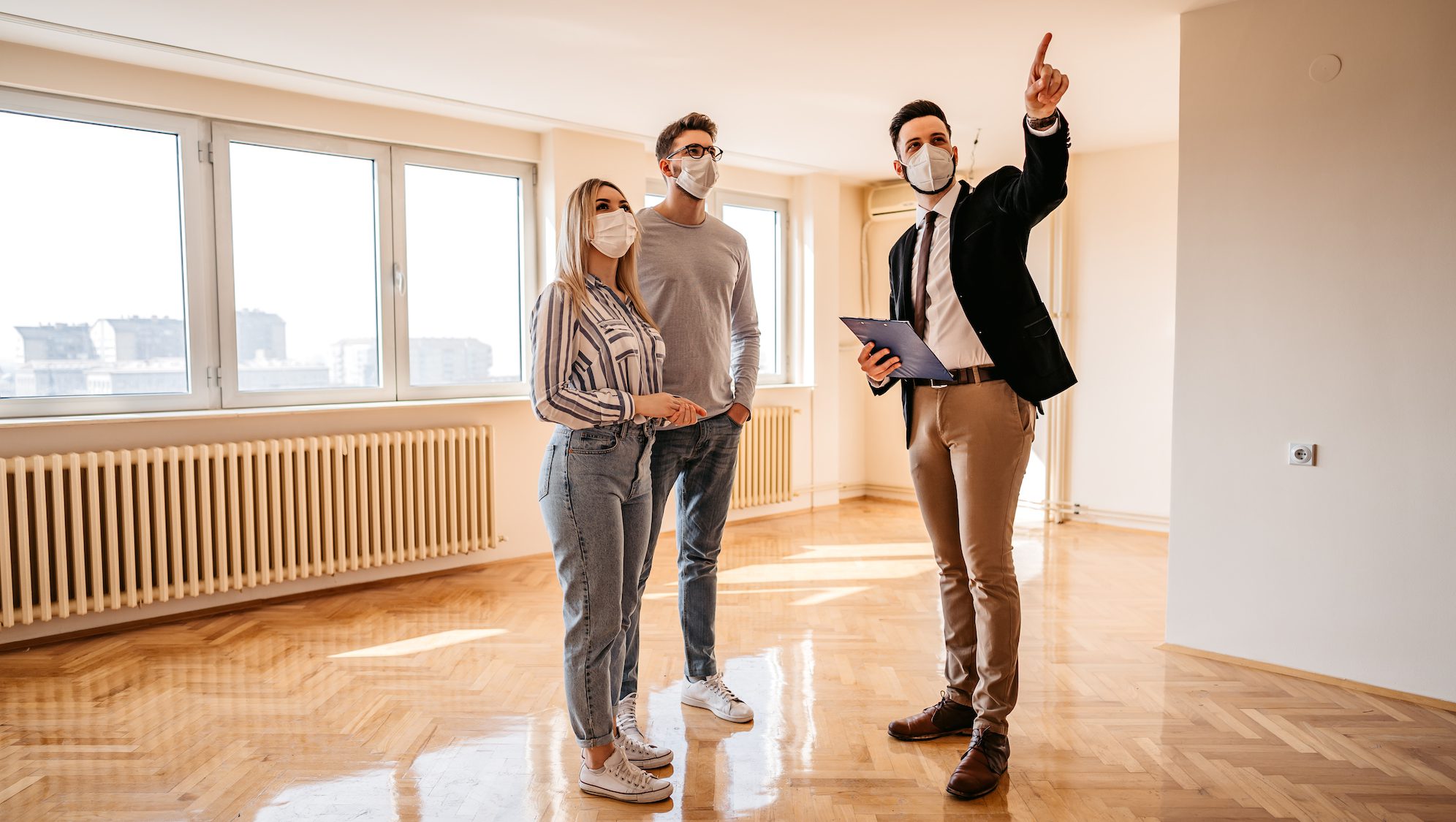 Young couple and male agent wearing face masks while looking a new real estate